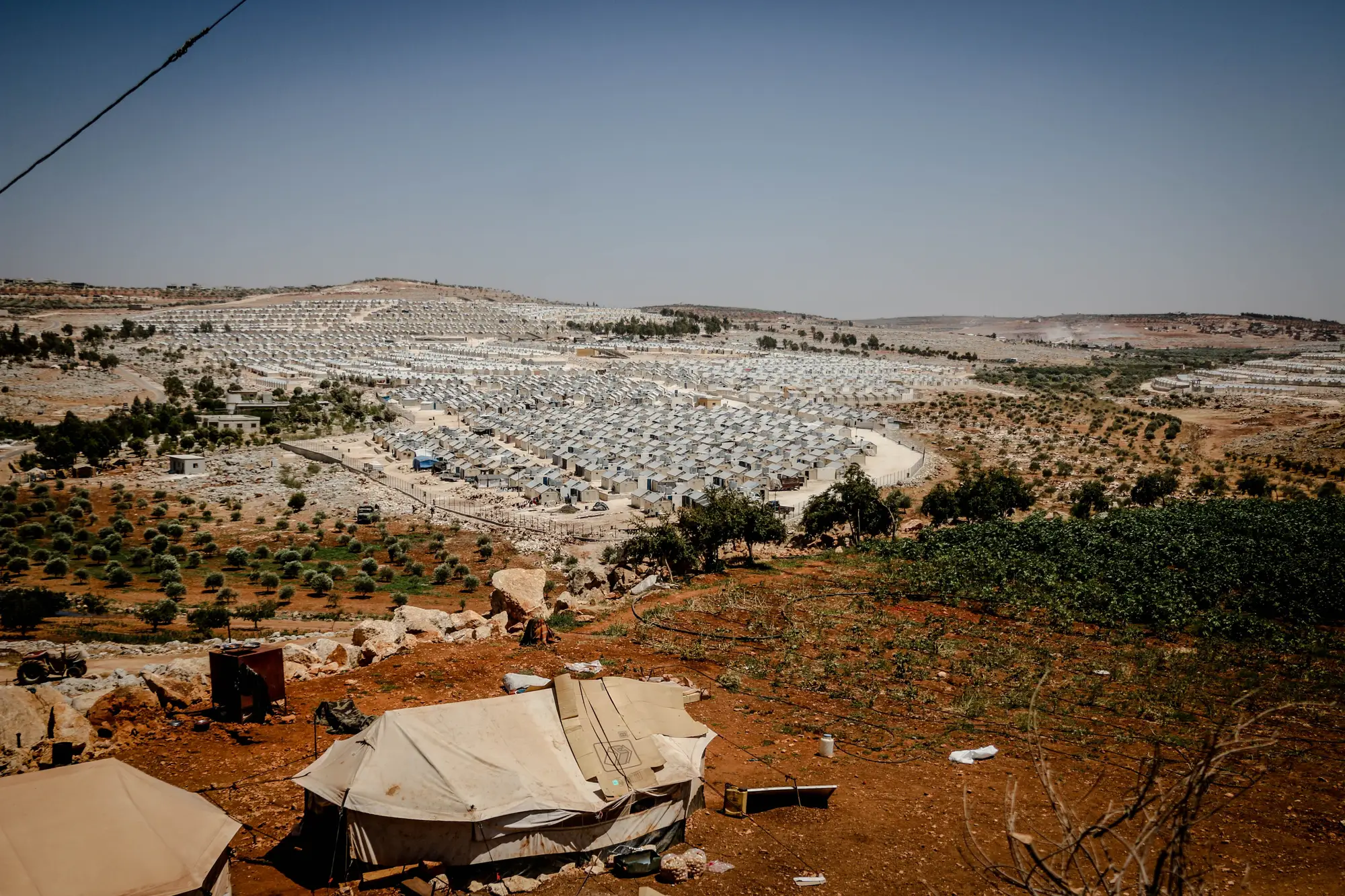 A tented settlement spreading across a dry hillside, seen from the ground at its edge